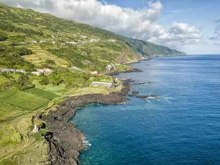 Aerial shot showing the small village of Manadas and the blue waters of the Atlantic ocean on Sao Jorge, Portugal.の写真素材