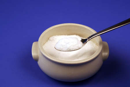 Bowl of sugar on a blue background with spoon
