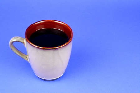 Brown coffee mug filled with coffee on a blue background