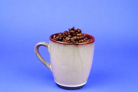Brown coffee mug filled with coffee beans on a blue background