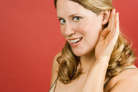Young woman on red with hand behind ear listeningの写真素材