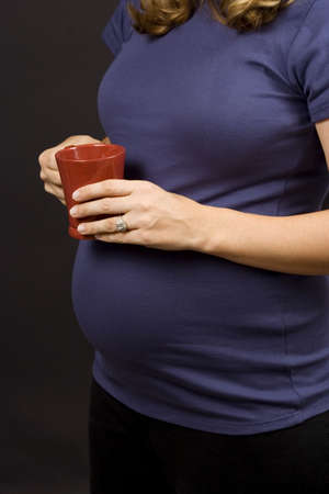 Pregnant woman on black holding a coffee mugの写真素材