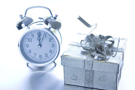 Wrapped gift and silver alarm clock on silver background.