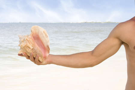 Attractive man at the beach holding a sea shell.の写真素材