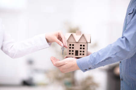 Female hand giving keys from new apartment to male hand on backgroundの写真素材