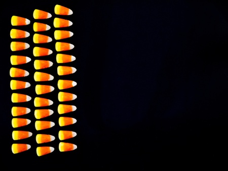Candy corn on black background.  Three rows on left half of field, points right.の写真素材