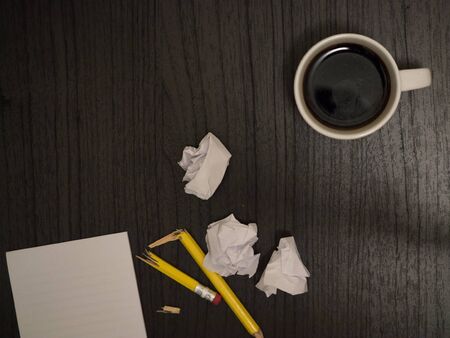 Dark surface, white,crumpled paper broken pencil, coffee, frustrationの写真素材