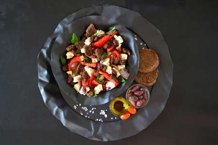 Dakos salad plated on a black tray with carob barley rusks, feta, tomato, olives, basil and olive oilの写真素材