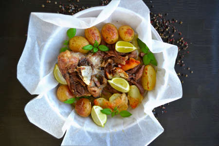 Plated kleftiko lamb dish cooked in cooking paper packages with vegetables and served with cheese and lemonの写真素材