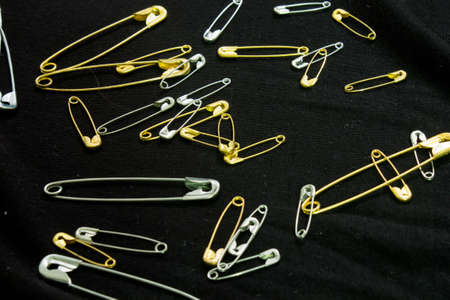This is a photograph of Silver and Gold safety pins placed on a black piece of fabricの写真素材