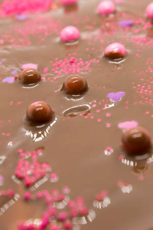 This is a photograph of Milk chocolate topped with round and heart shaped Pink and Purple sprinkles