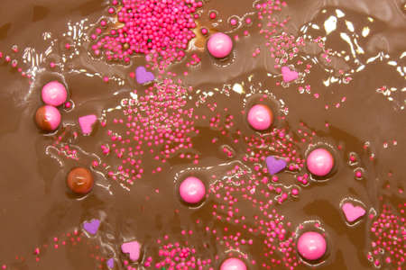 This is a photograph of Milk chocolate topped with round and heart shaped Pink and Purple sprinkles