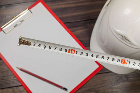 White hardhat, pencil and a tape-line on a wooden background illustrating construction mesurementsの写真素材