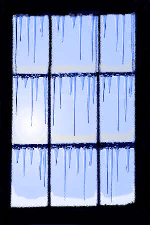 window in the cold season with icicles and sun lightの写真素材