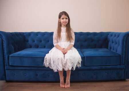 a beautiful girl sits on a blue sofa and looks sadの写真素材