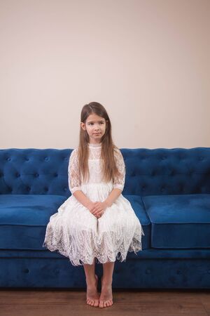 the girl is sitting on a blue sofa in a bright room and posingの写真素材