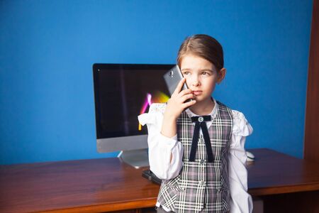 a girl in a business suit stands at the computer and talks on the phone