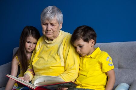 An old grandmother and her beloved grandchildren sit at home and read an interesting bookの写真素材