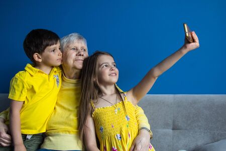An old grandmother and her beloved grandchildren sit at home and take photos on their smartphoneの写真素材