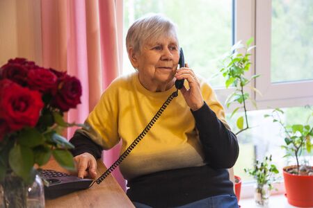 Grandmother is on the phone sitting in a chair in a cozy room with flowersの写真素材