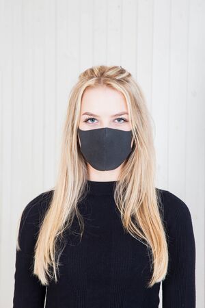 blonde beauty in a black bodysuit and a black protective mask against a white wallの写真素材