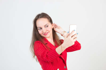 Portrait of a young woman in a red suit taking a selfie on her smartphoneの写真素材