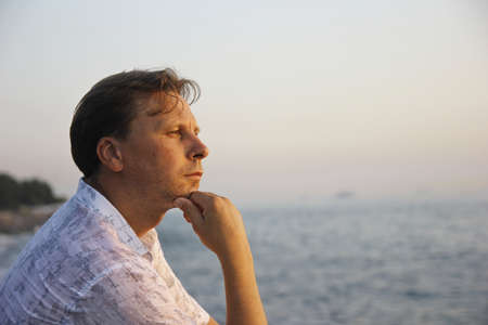 Middle-aged man sitting close to the sea and thinkingの写真素材