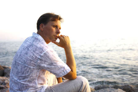 Middle-aged man sitting close to the sea and thinkingの写真素材