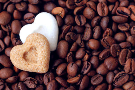 Brown and white sugar hearts lying on roasted coffee beansの写真素材