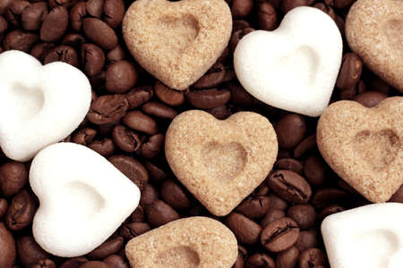 Brown and white sugar hearts lying on roasted coffee beansの写真素材