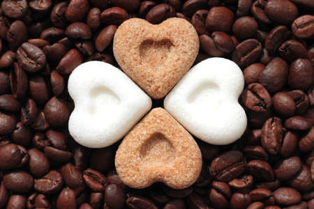 Brown and white sugar hearts lying on roasted coffee beansの写真素材