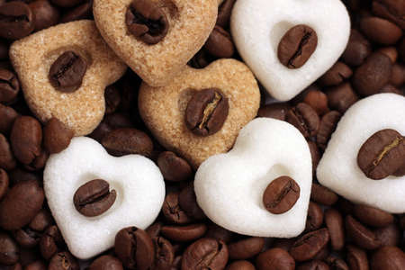 Brown and white sugar hearts lying on roasted coffee beansの写真素材