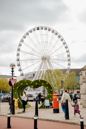 Liverpool, UK, April 11 2024: Decorative Easter objects are placed on the sidewalk, near the Wheel Of Liverpool located on the Waterfront Pier Head Promenade Liverpool. Passers-by stop and take photos in the created setting.のeditorial素材