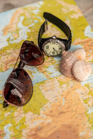 Sunglasses and watch on a map with seashells.