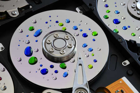 Closeup of open hard disk drive with colored drops over