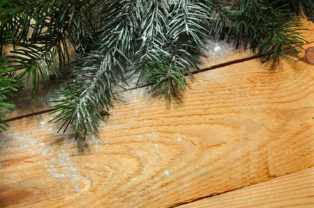 Snow-covered Christmas tree branch on wood. Christmas background