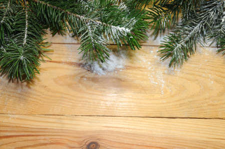 snow-covered Christmas tree branch on wooden background. Xmas background frame