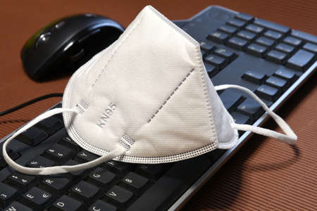 Smart working during Covid-19 or Coronavirus disease. Computer keyboard, mouse and protection mask ffp2 against covid-19 on a brown background.の写真素材