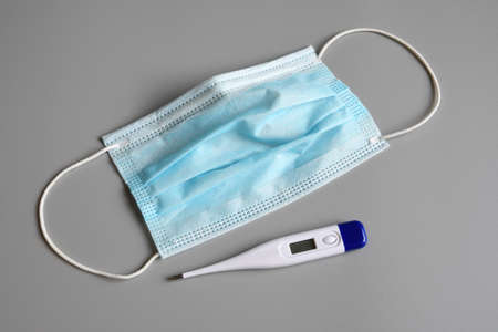 fever thermometer with blue surgical mask on gray background, against pandemic disease, outbreak, Covid 19 concept.の写真素材