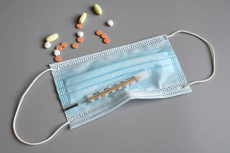fever thermometer over blue surgical mask on gray background with medicines against pandemic...