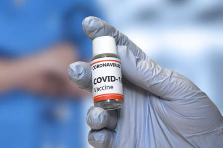 Coronavirus Vaccine concept. Hand of doctor with blue glove hold a vaccine jar against Covid-19....