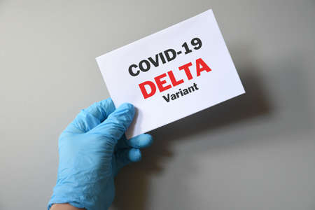 Doctor's hand in blue glove with white paper and text Covid-19 Delta Variant. Concept of medical variety delta variant and COVID-19. Concept words 'delta variant'. COVID-19 delta variant concept.の写真素材