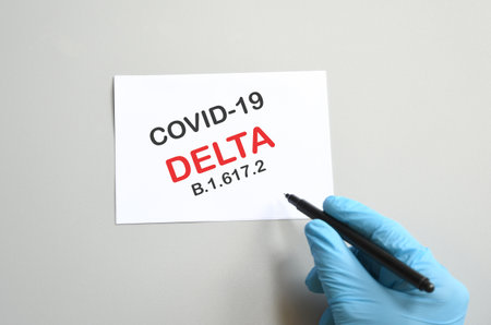 doctor hand with blue glove writes on white paper the text delta Covid-19 variant B.1.617.2, medical delta variant strain concept and COVID-19. Copy space.の写真素材