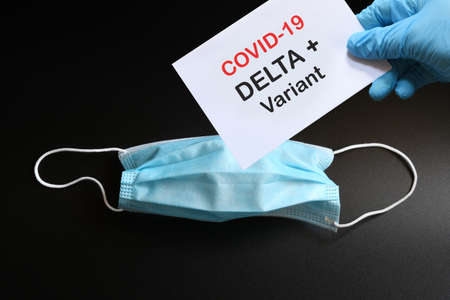 Doctor's hand in blue glove with white paper and text Covid-19 Delta + Variant with antiviral medical mask on background. COVID-19 delta variant strain concept.の写真素材