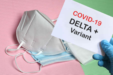 Doctor's hand in blue glove with white paper and text Covid-19 Delta + Variant with various protection masks on background. COVID-19 delta variant strain protection concept.の写真素材