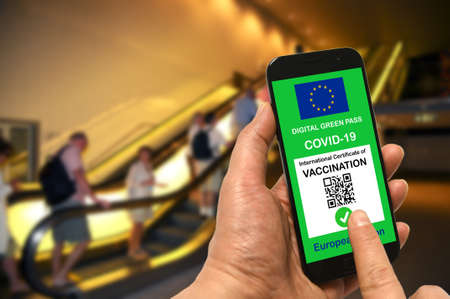 A man in a shopping mall holds a smartphone with the European Union digital green pass for Covid-19 in his hand. Safety concept for Coronavirus and the Green passの写真素材