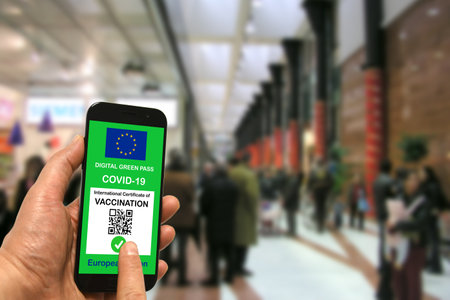 A man in a shopping mall holds a smartphone with the European Union digital green pass for Covid-19 in his hand. Safety concept for Coronavirus and the Green passの写真素材