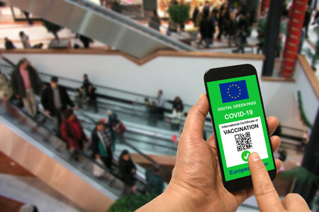 A man in a shopping mall holds a smartphone with the European Union digital green pass for Covid-19 in his hand. Safety concept for Coronavirus and the Green passの写真素材