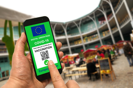 A man in a shopping mall holds a smartphone with the European Union digital green pass for Covid-19 in his hand. Safety concept for Coronavirus and the Green passの写真素材