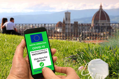 The digital green pass of the European Union with the QR code on the screen of a hand-held mobile phone with a mask and tourists admiring the Cathedral of Florence, Italy.の写真素材